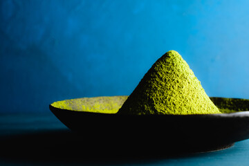 Japanese traditional green tea (matcha) powder in a heap on a black round plate against a blue design board.