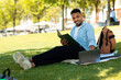© Prostock-studio - Happy black guy writing some notices in notebook and preparing for exam with laptop, sitting in city park