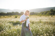 © morrowlight - Attractive blonde female girl pick up camomile flower walk in field over green nature outdoor. Beautiful woman holding chamomile bouquet in meadow over sun light outside. Spring season.