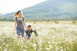 © morrowlight - Cute beautiful young woman holding hands and play with little child girl walk in chamomile field with blooming flowers over nature background. Family lifestyle concept. Mom and baby daughter in grass