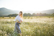© morrowlight - Attractive blonde female girl pick up camomile flower walk in field over green nature outdoor. Beautiful woman holding chamomile bouquet in meadow over sun light outside. Spring season.