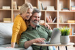 © Prostock-studio - Happy middle aged couple websurfing on laptop together while relaxing at home