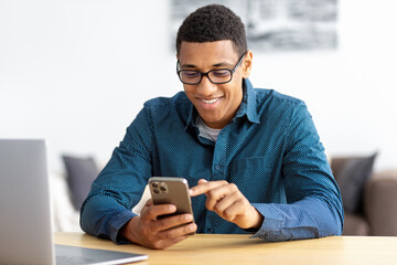 Young African American man entrepreneur in modern office looking at screen typing message with mobile phone Smiling male in workplace using smartphone search the Internet or chatting in social network