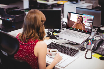 Poster - Caucasian businesswoman holding coffee cup video conferencing with coworker over laptop in office