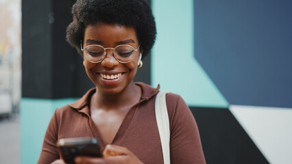 african woman walking in the city using her smartphone and smili