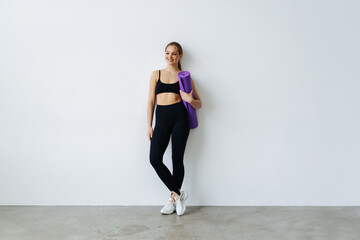 Young woman holding a yoga mat, isolated in a white background