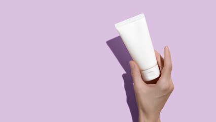 Wall Mural - Young female hands holding blank white squeeze bottle plastic tube on pink background. Packaging of cream, lotion, gel, facial foam or skincare. Cosmetic beauty product branding mock-up. Copy space