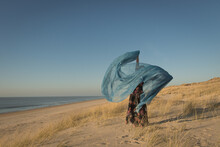 Woman In Floral Dress Dancing On The Beach Hlding Fabric In The Wind
