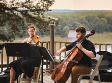 Female Violin Player And Male Cello Player Playing Duet On Wooden Deck Over Missouri River On Summer Evening