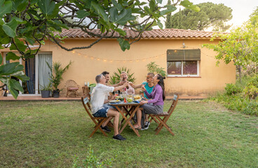 Happy friends dining and tasting together in garden in barbecue dinner party in summer. Smiling people eating at house patio. Smiles, cheerfulness concept.