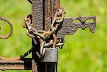 The Rusty Gate Is Locked With A Padlock With A Chain.