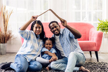 Portrait Enjoy Happy Smiling Love Black Family African American Father And Mother With Young Parents Little Asian Girl Sitting And Making Roof House With Hand Arm Over Head In New Home