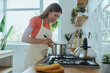 © gstockstudio - Confident young woman cooking soup while standing at the domestic kitchen