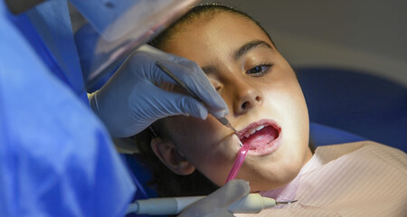 Sticker - Young caucasian female smiling while dentist in white latex gloves check condition of her teeth. baby girl in blue dental chair