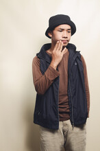 Portrait Of Asian Youth With Disappointed Pose Wearing Hat, Brown T-shirt And Black Vest Isolated On Background