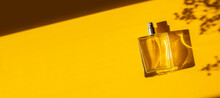 Transparent Bottle Of Perfume On A Yellow Background. Fragrance Presentation With Daylight. Trending Concept In Natural Materials With Beautiful Shadow. Women's Essence.