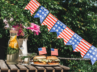 Two delicious burgers, homemade lemonade, vase with bright flowers, pattern in the form of stars and stripes. Close-up, outdoors. Day light. Concept of holidays and delicious food