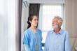 © chartphoto - Portrait of an asican young nurse helping old elderly  man grandfather to walk  in the bedroom. Senior patient of nursing home moving with walking frame and nurse support