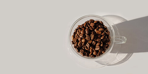 Glass cup full of coffee beans with sunlight and shadow on white backgraund, bunner top view