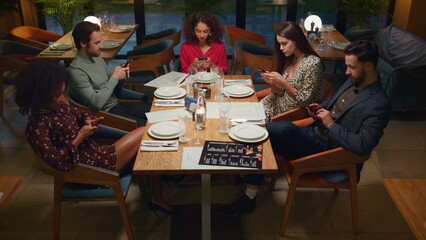 Multiracial group checking phone device in cafe. Friends texting in restaurant.