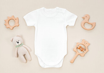 white baby bodysuit for mockup on a pastel beige background. baby wooden teethers and crocketed toy 
