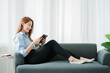 © ArLawKa - beautiful asian woman sitting on the sofa with a tablet At home, in the living room, video call with friends over the Internet.