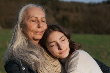 Wall Mural - Happy senior grandmother with teenage granddaguhter hugging in nature on spring day.