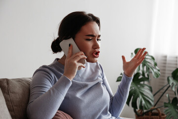 Portrait of irritated young woman arguing on phone. Outraged female talking angrily, shouting at cellphone. Customer support frustration concept. Copy space for text, white wall background, close up.