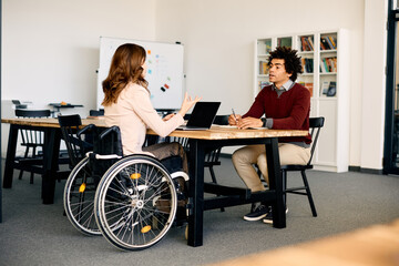 Wall Mural - Disabled businesswoman working on laptop and talking to male colleague i office.