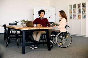 Happy black businessman talks to female colleague with disability in office.