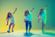 Leinwandbild Motiv Group of children, little girls in sportive casual style clothes dancing in choreography class isolated on green background in yellow neon light. Concept of music, fashion, art