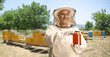 Bee keeper in a uniform holding a honey jar on a bee farm