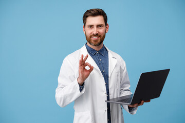 Smiling medical specialist in a white coat holding laptop and showing okey sign