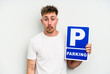 Young caucasian man holding parking placard isolated on white background shrugs shoulders and open eyes confused.