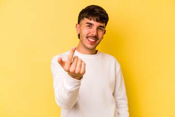 Wall Mural - Young caucasian man isolated on yellow background pointing with finger at you as if inviting come closer.