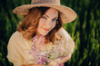 © Cavan Images - Pretty countryside woman in straw hat with flowers bouquet in field.
