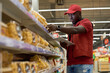 © pressmaster - Young male shop assistant in uniform checking prices of packed cookies or chakchak and entering them into database in digital tablet