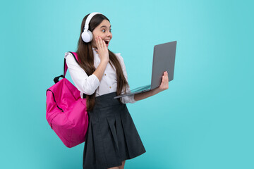 Wall Mural - Back to school. Happy teenager school girl in school uniform with bagpack, headphones and laptop. School children on isolated blue background. Excited face. Amazed expression