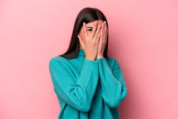 Wall Mural - Young caucasian woman isolated on pink background blink through fingers frightened and nervous.