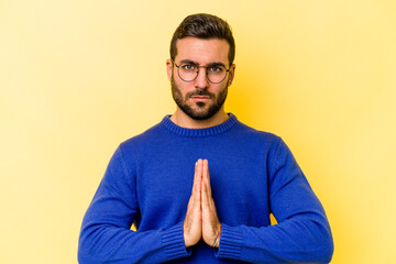 Young caucasian man isolated on yellow background praying, showing devotion, religious person looking for divine inspiration.