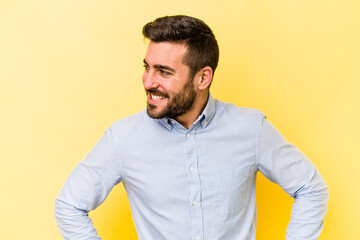 Wall Mural - Young caucasian man isolated on yellow background laughs happily and has fun keeping hands on stomach.