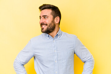 Wall Mural - Young caucasian man isolated on yellow background confident keeping hands on hips.