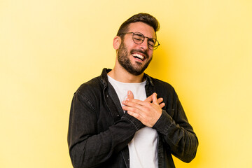 Wall Mural - Young caucasian man isolated on yellow background laughing keeping hands on heart, concept of happiness.