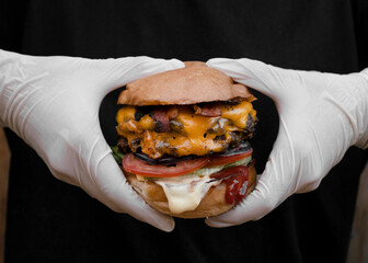 Monster burger. Closeup view of chef hands holding and showing a mega burger with two meat medallions, cheddar cheese, lettuce, tomato, ketchup and mayonnaise.