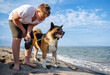Teenage guy with blond hair and leash in hands plays and walks with dog of Akina Inu breed on wild beach along Black Sea