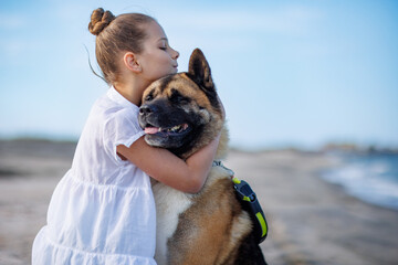 Teenage girl in light clothes hugs and loves dog friend of Akita Inu breed on beach near Black Sea in warm sunny weather