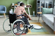© Seventyfour - Full length portrait of modern black man with disability using robot vacuum cleaner and smart home technology, copy space