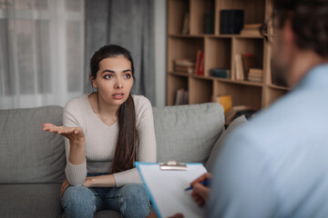 Wall Mural - Sad dissatisfied caucasian millennial female patient talking with psychologist man in office clinic interior