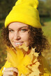 Young smiling woman with autumn leaf has fun in the autumn park. Portrait of curly hair happy woman on the foliage outdoors.