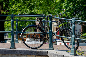 Wall Mural - Vintage classic bicycle parked along the canal bridge of Amsterdam with blurred traditional houses as background, Cycling is a common mode of transport in Holland, Netherlands land of bicycle.